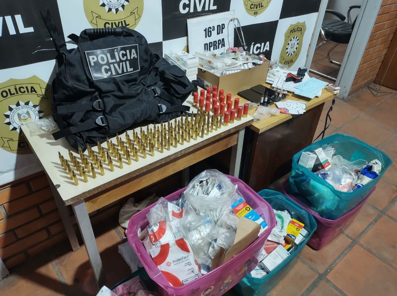 Materiais apreendidos expostos em mesa e ao chão com banner da Polícia Civil