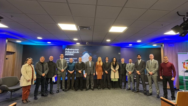 Participantes do encontro em pé posados para foto em frente ao banner do evento