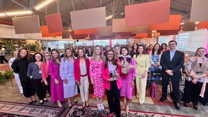 Dezenas de mulheres em pé, vestindo majoritariamente rosa, posadas para foto coletiva