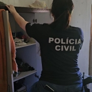 Policial civil mulher de costas, com camiseta preta com inscrições: Polícia Civil, fiscalizando residência