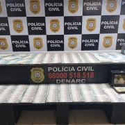 Diversos c&eacute;dulas de reais espalhadas sobre mesas e ao fundo banner da Pol&iacute;cia Civil