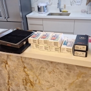 Aparelhos eletr&ocirc;nicos e caixas de eletr&ocirc;nicos expostos em bancada de cozinha no local da apreens&atilde;o