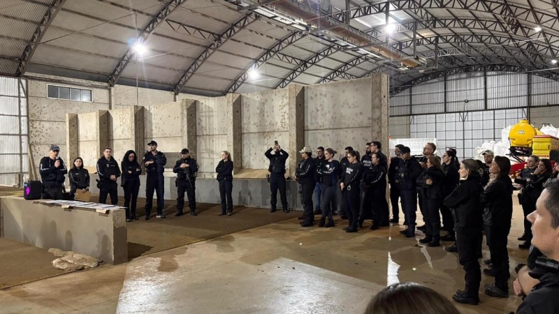 Diversos policiais civis vestindo pretos em um semic&iacute;rculo dentro de um grande galp&atilde;o, aparentando ser industrial