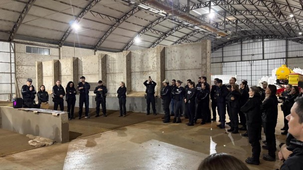 Diversos policiais civis vestindo pretos em um semic&iacute;rculo dentro de um grande galp&atilde;o, aparentando ser industrial