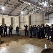 Diversos policiais civis vestindo pretos em um semic&iacute;rculo dentro de um grande galp&atilde;o, aparentando ser industrial