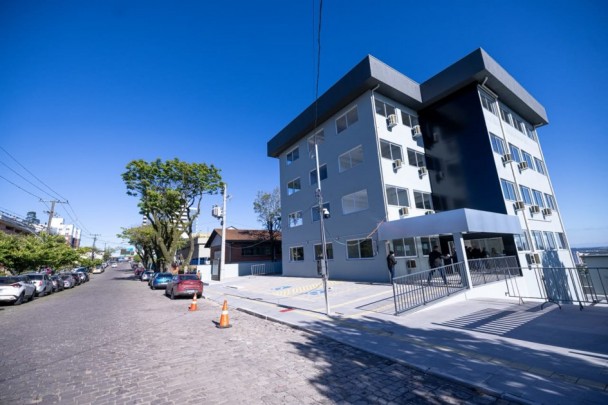 Vista externa de prédio de quatro andares com cores cinza e preto, mostrando também parte de rua e veículos estacionados